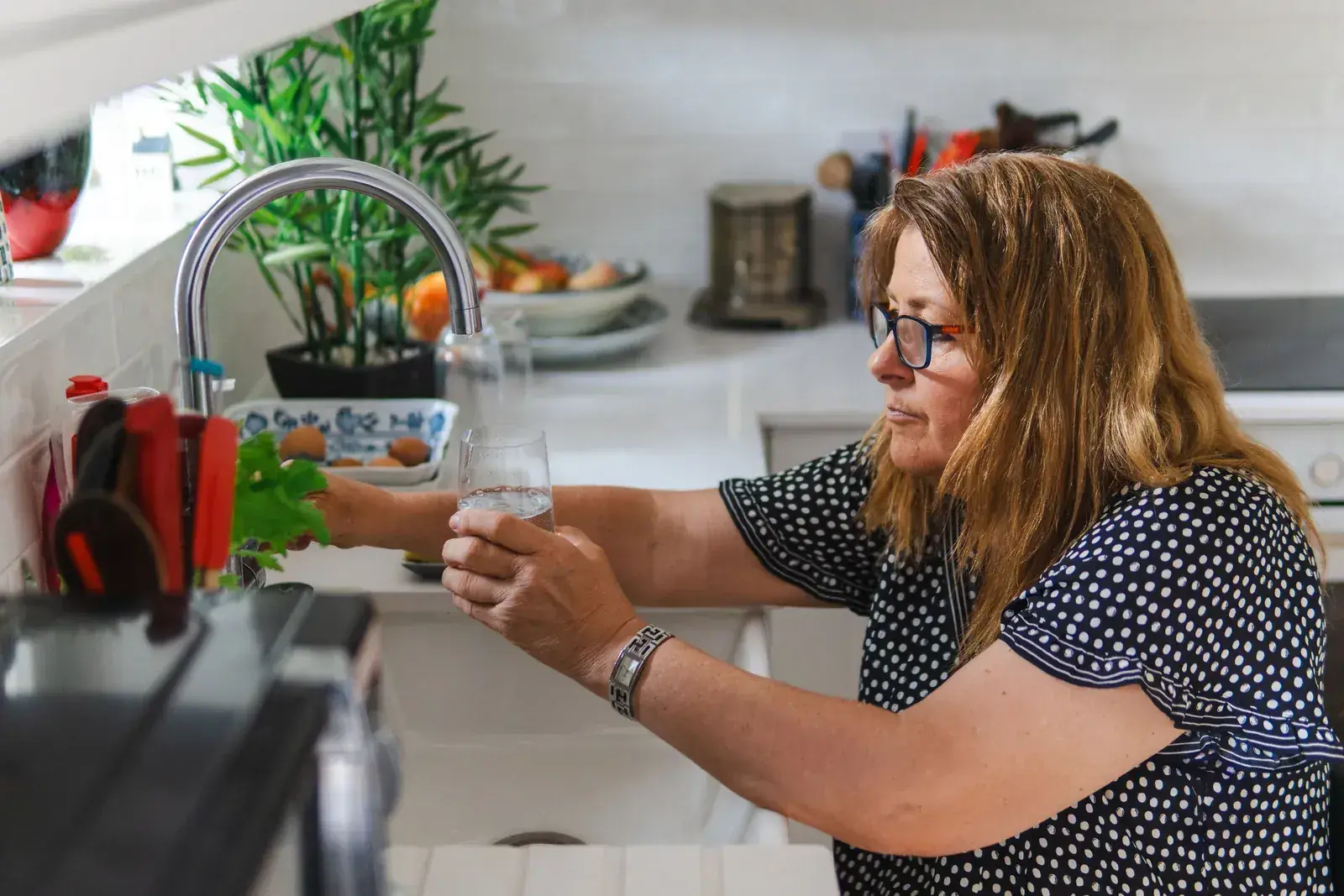 Une femme remplit un verre d’eau au robinet de sa cuisine.